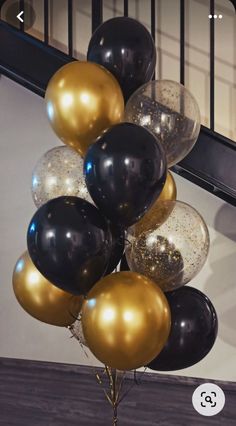 a bunch of black and gold balloons hanging from a stair case in front of a staircase