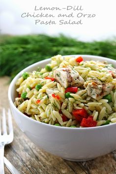 a white bowl filled with pasta and chicken on top of a wooden table next to silverware