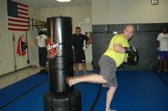 a man in yellow shirt and gray shorts kicking a punching bag