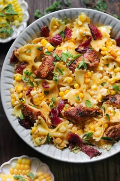 a white plate topped with pasta and meat next to corn on top of a wooden table