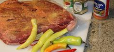 a large piece of meat sitting on top of a cutting board next to peppers and seasonings