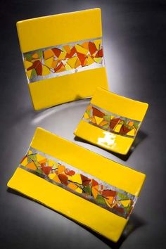 three pieces of yellow glass with colorful designs on the bottom and sides, sitting next to each other