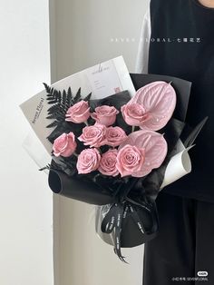 a woman holding a bouquet of pink roses in front of a white wall with an envelope