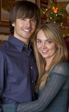 a young man and woman standing next to each other in front of a christmas tree