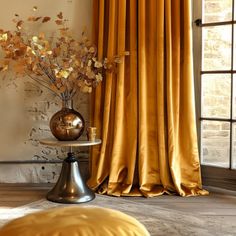 a vase with flowers on top of a table next to a window covered in yellow drapes