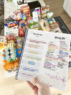 a person holding up a recipe book in front of a table full of snacks and condiments