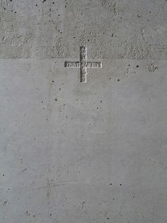 a cross on the side of a cement wall, with small holes in between it