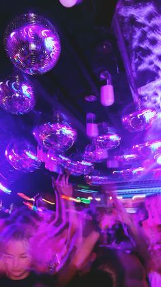 people are dancing at a party with disco balls hanging from the ceiling and purple lighting