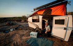 a man sitting in the doorway of a camper with an orange tarp over it