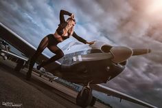 a beautiful woman standing next to an airplane on top of a tarmac with clouds in the background