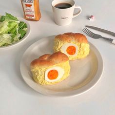 two eggs in bread are on a plate next to a cup of coffee and salad