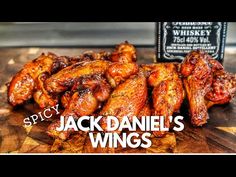 a pile of chicken wings sitting on top of a wooden cutting board next to a bottle of whiskey