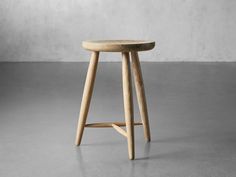 a wooden stool sitting on top of a cement floor in front of a white wall