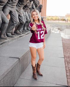 a woman wearing a football jersey and cowboy boots posing for a photo in front of a statue