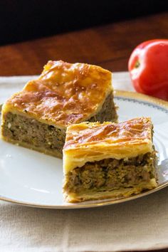 two slices of meat and vegetable pie on a plate with an apple in the background