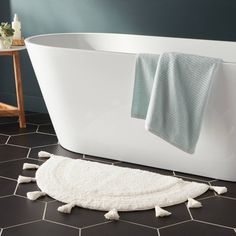 a white bath tub sitting on top of a black tiled floor next to a rug