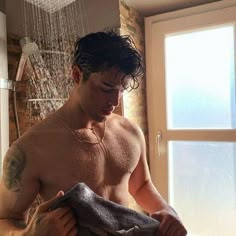 a shirtless man is drying his hands in the shower while looking down at something