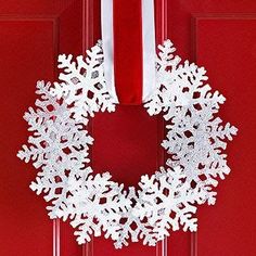 a white snowflake wreath hanging on a red door with a red velvet ribbon