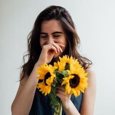 a woman holding a bouquet of sunflowers in her hand and covering her mouth