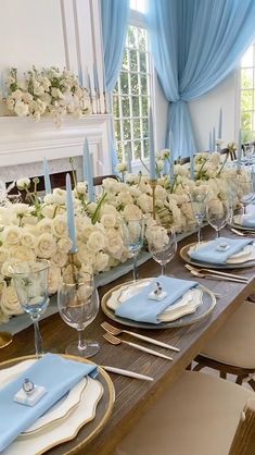 a long table set with white flowers and blue napkins, silverware and place settings