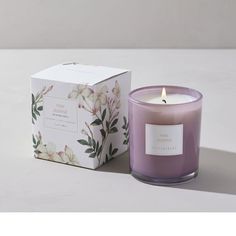 a purple candle sitting next to a box on a table with a white flower design