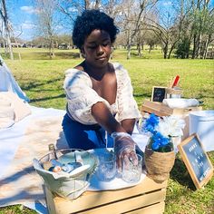 a woman is sitting at a table with flowers and jars in front of her on the grass