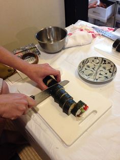 a person cutting up sushi on top of a white table