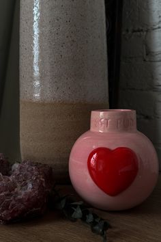 a pink vase with a red heart on it next to a rock and planter