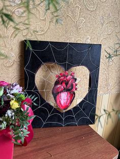 a heart in a spider web frame on a table next to a vase with flowers