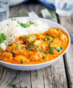 a white bowl filled with rice and chicken curry next to a glass of water on a wooden table