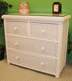 a white wicker dresser next to a green wall with a clock on the top