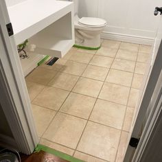 a white toilet sitting in a bathroom next to a sink and a wooden floor with green tape on it