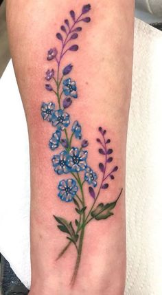 a blue flower tattoo on the left arm and leg, with purple flowers growing out of it