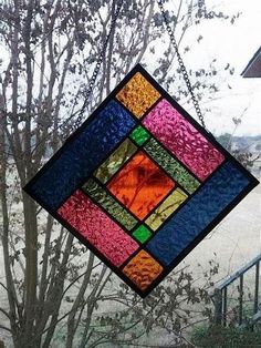 a stained glass window hanging from the side of a tree in front of a house