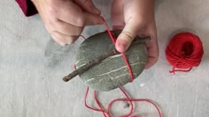 someone is making a rock with yarn on the ground next to it and two balls of red string