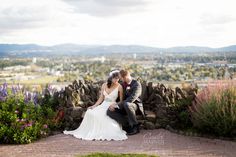 a bride and groom are sitting on a stone wall