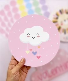 a hand holding up a pink card with a cloud on it and hearts hanging from the clouds