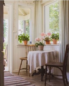 a dining room table with flowers in pots on the windowsill and an open door