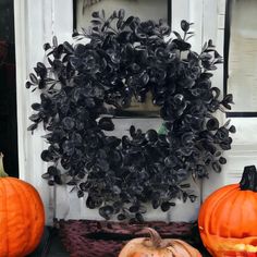 two pumpkins sitting in front of a door with a wreath on it's side