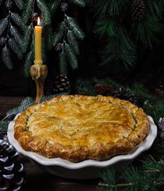 a pie sitting on top of a white plate next to pine cones and a candle