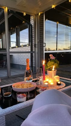 an outdoor dining area with candles, plates and glasses on the table in front of large windows