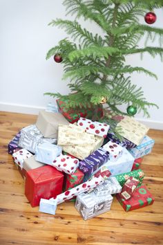 a christmas tree with presents under it on the floor next to a pile of wrapped gifts