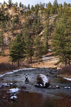 two people are wading through a stream in the mountains