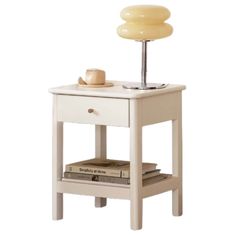 a small white table with a lamp on top and some books underneath the end table