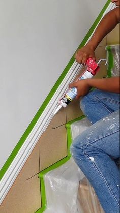 a woman sitting on the ground painting a wall with green tape and paint rollers