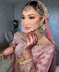 a woman in a pink outfit with jewelry on her head and hands near her face