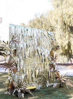 an outdoor sculpture made out of tin foil and flowers in the grass with trees behind it