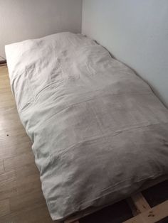 an unmade bed sitting on top of a wooden floor next to a white wall