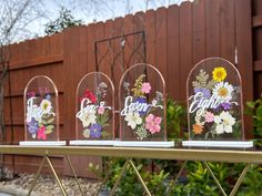 three clear vases with flowers on them sitting on a gold table in front of a fence