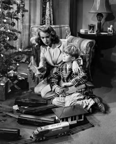 a woman sitting next to a child near a christmas tree